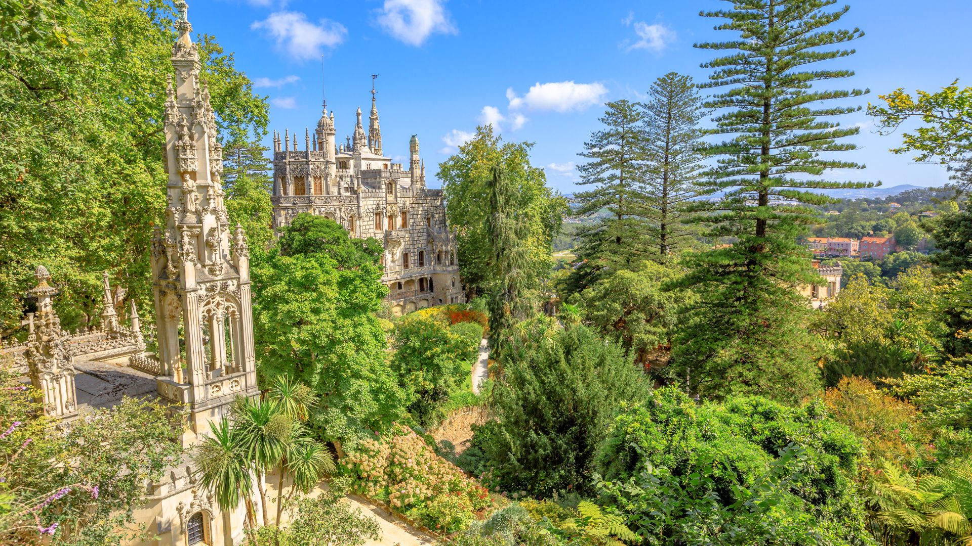 Aerial view of the lush gardens at Quinta da Regaleira, with the palace partially visible among tall trees and greenery.