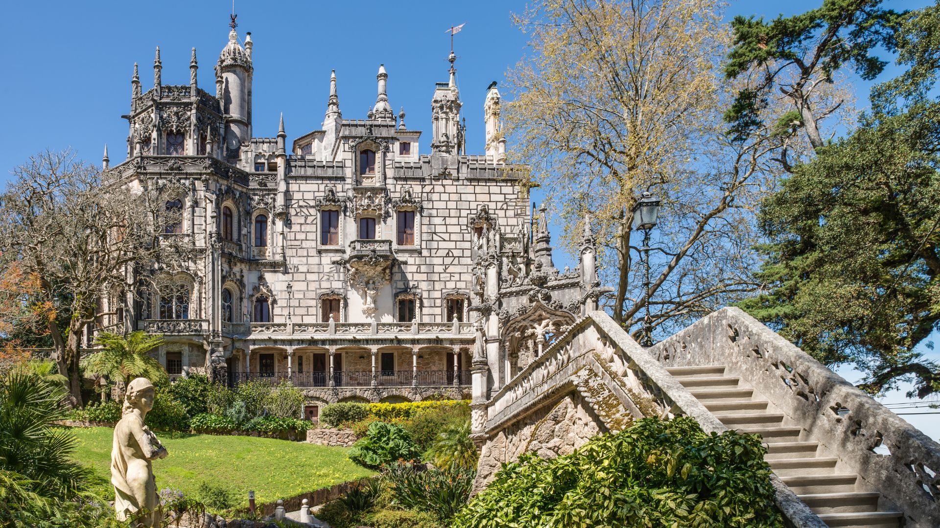 The ornate façade of the Quinta da Regaleira Palace in Sintra, Portugal, surrounded by lush gardens and stone staircases.