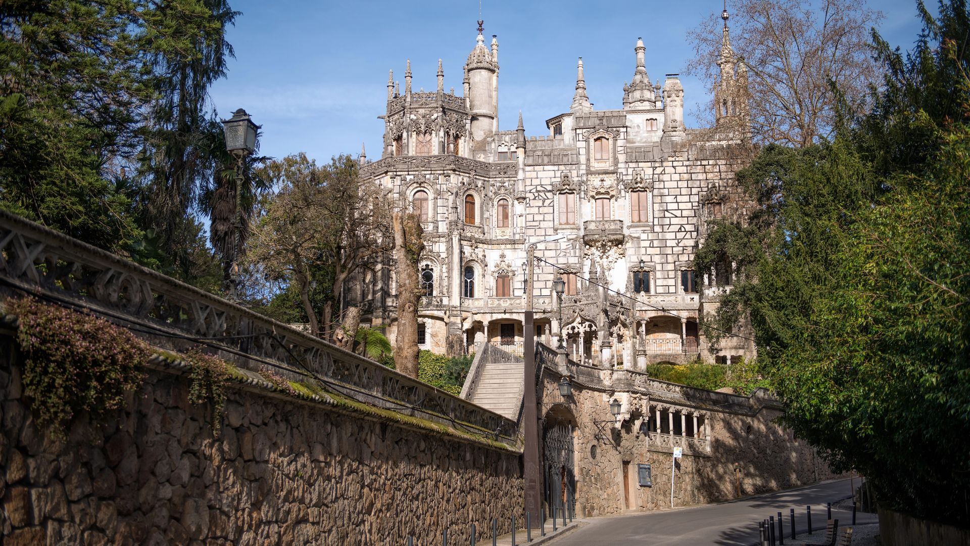 Street-level view of the main entrance to the Quinta da Regaleira Palace in Sintra, with stone walls and a grand staircase.